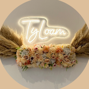 Texte lumineux "TyLoam" entouré de fleurs et de pampas.