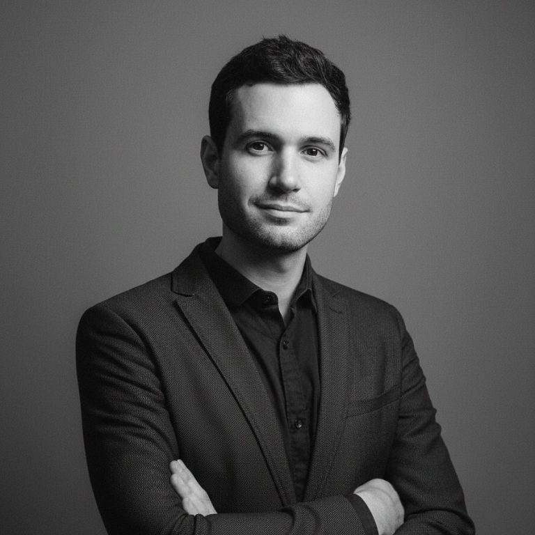 Un homme en costume noir se tenant avec les bras croisés, sur fond gris.