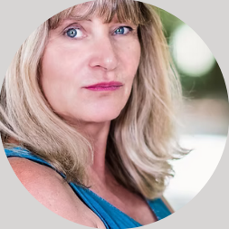 Femme d'âge moyen avec les cheveux blonds, portant un débardeur bleu, regard pensif.